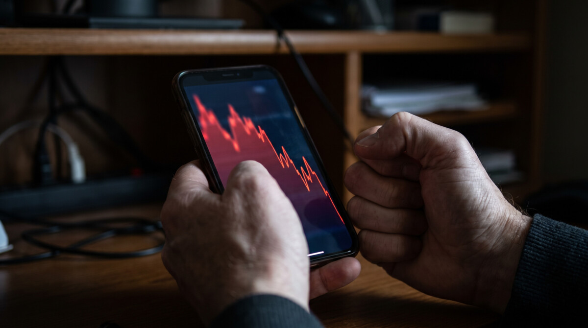 Common investing mistakes beginners make — hands gripping phone showing volatile stock chart during market panic