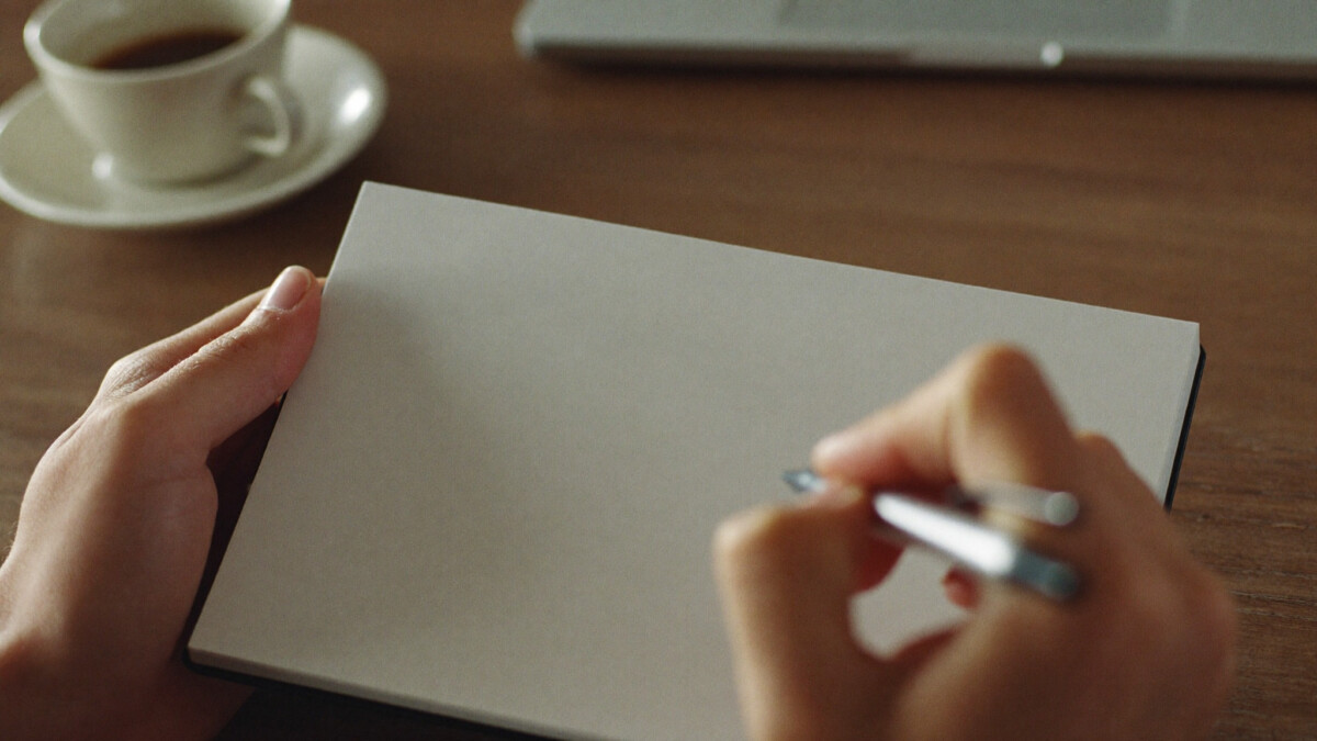 hands holding a pen over a blank notepad while planning a freelance project scope