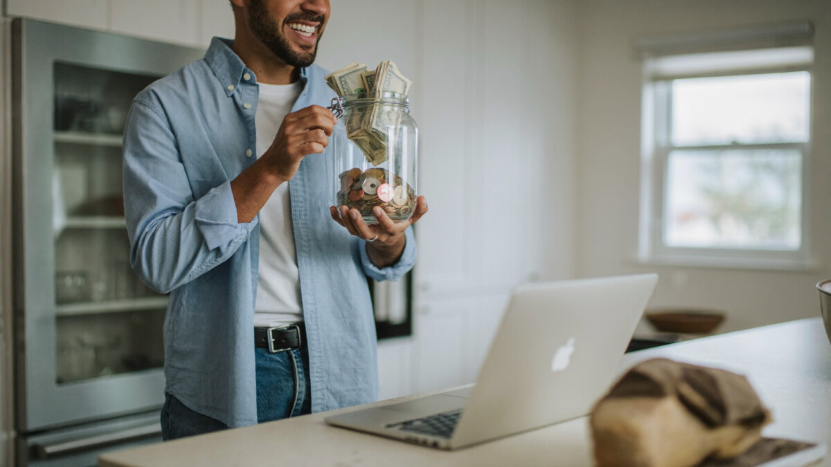 Man holding a jar of savings next to a laptop after choosing to invest $500
